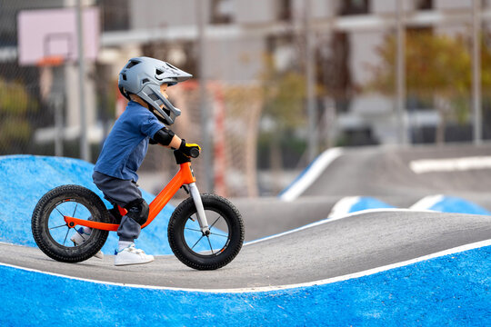 Young boy in helmet and protective gear riding an orange balance bike on a pump track