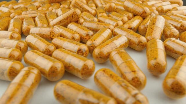 Numerous turmeric capsules are displayed in close up, emphasizing their organic powder content and transparent shells. The image represents modern health and holistic nutrition concepts