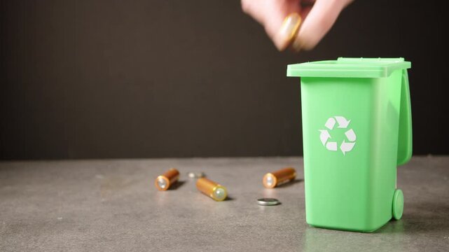 Female hand putting used batteries into special green recycling bin