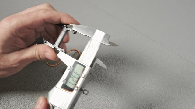 An engineer works with a digital caliper to measure a small robotic servo component with gears and wiring. Taking size, wide, length The precise measurement is shown on the LCD screen of the tool.