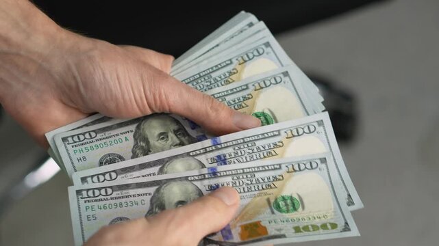 A person counts a stack of crisp US hundred dollar bills, emphasizing financial success and economic security. The scene highlights themes of money management, investment, and prosperity