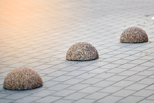 Concrete hemisphere bollards on grey sidewalk paving. Urban traffic safety barriers for pedestrian protection. Durable pebble stone texture on concrete obstacles. Pedestrian zone restriction