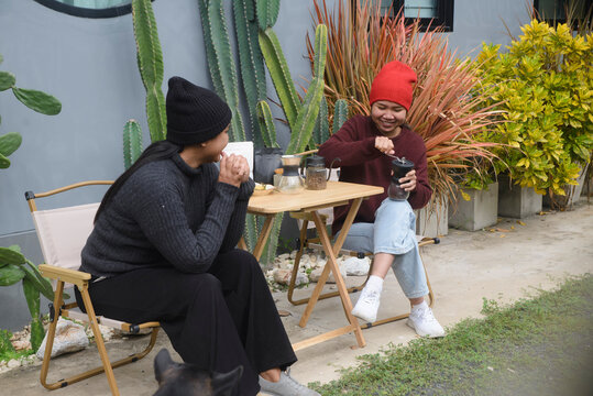 Coffee drip camping friend woman, brewing hot coffee together on foldable wooden table with cactus garden background, during outdoor winter leisure activity in cozy home backyard for lifestyle concept