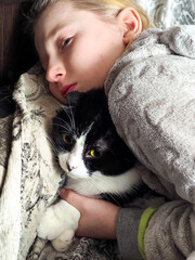 Tender moment of a teenage girl hugging her tuxedo cat wrapped in a cozy fleece blanket at home. Concept of pet affection, emotional support, home comfort, and unconditional love. © parovysh