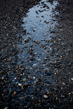 Water trickles through stones on a beach during sunset near the shore