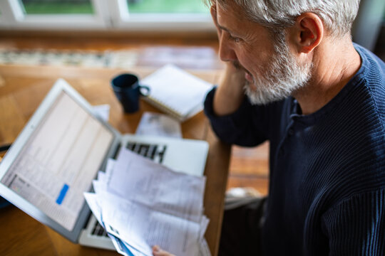 Man reviewing bills and receipts on laptop at home