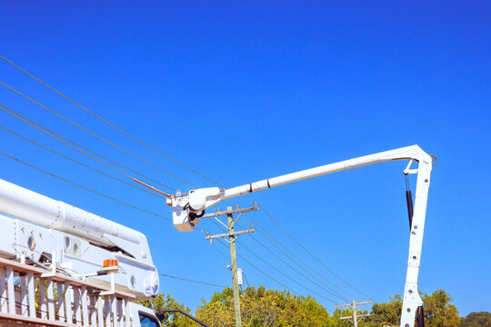 An aerial lift extends toward power lines above utility truck on power line works