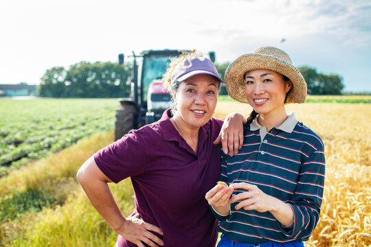 Two women farmers holding wheat in field with tractor