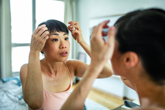 Woman checking her hairline in a bedroom mirror