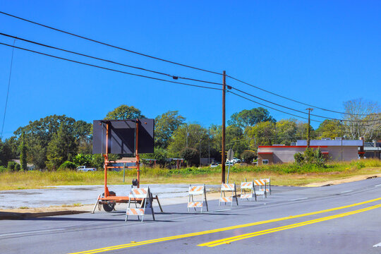 Temporary signs mark road work beside two lane road, with utility lines low building in background.