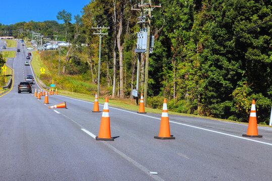 Orange cones guide vehicles past road work on two lane road beside utility poles.