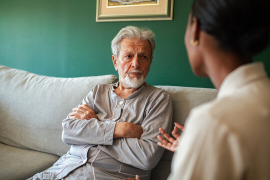 Elderly man with crossed arms listening to woman at home