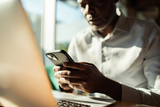 Man using smartphone while working on laptop at desk