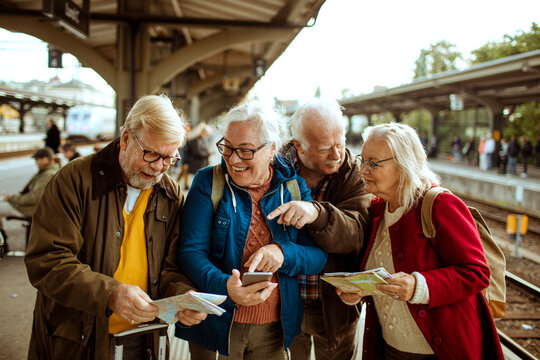 Senior friends checking maps and phone at train station