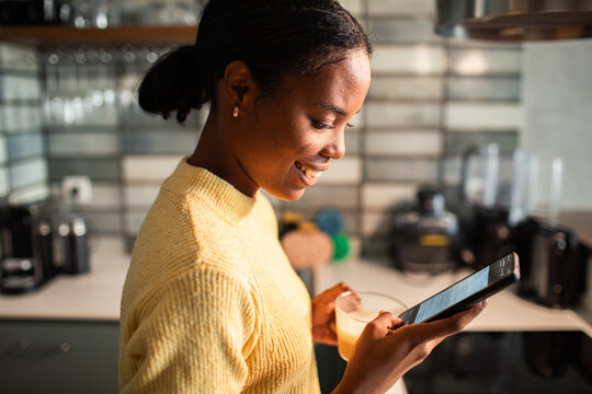 Woman texting on smartphone while holding drink in kitchen