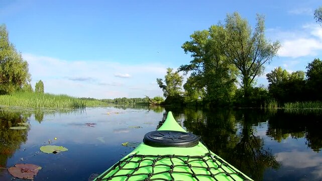 Forward view green kayak bow floating near green river bank trees and floating lily pads