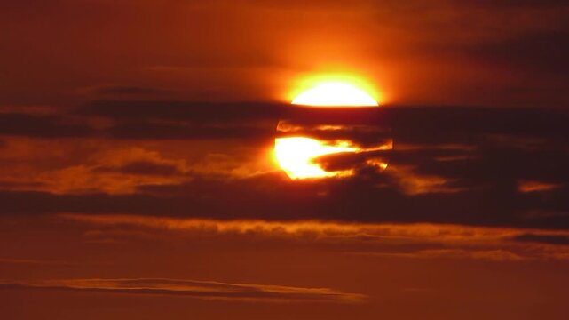 Golden big sun disk is setting behind dark clouds over ocean in the sky