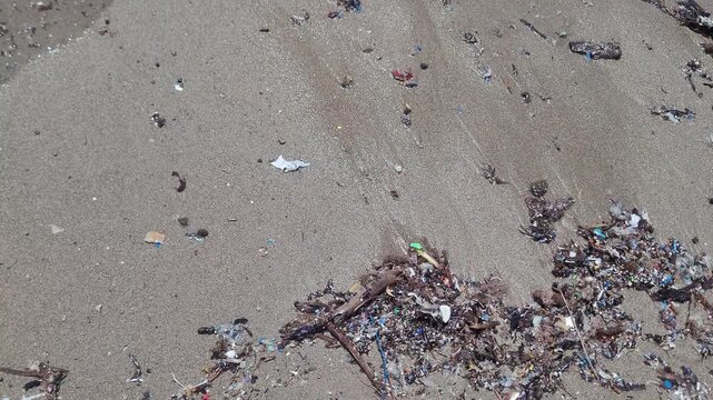 Close-up of plastic microplastics and ocean debris washed up on a sandy shoreline.