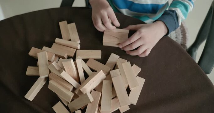 Close-up children's hands play with wooden bricks constructing structures. 4K 10-bit