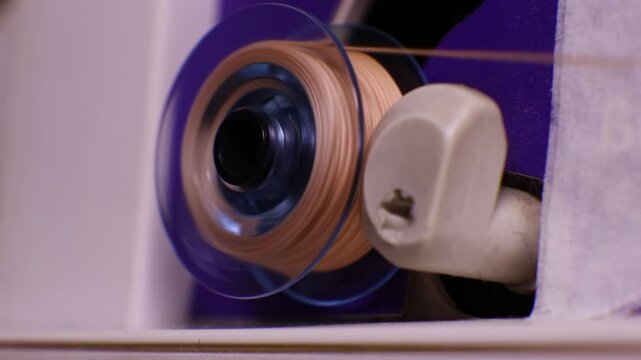 Close-up view of a sewing machine bobbin being wound with thread. The image captures the rapid movement of the spool as thread is evenly wrapped around it, essential for the machines stitching.