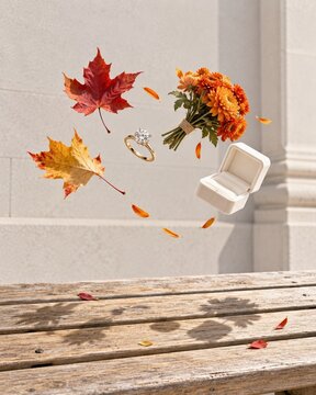 Fall engagement ring and autumn leaves floating in a dynamic arc over a weathered wooden bench for jewelry advertising and wedding articles