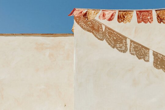 Papel picado flags in coral and brown hanging against a textured lime wall with crisp shadow patterns and copy space for Day of the Dead