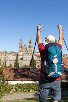A pilgrim on the Camino de Santiago raises his hiking poles in front of the Cathedral of Santiago, celebrating the end of his journey. Copy space
