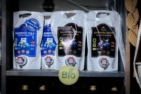 Limbazi, Latvia - October 21, 2026: Organic berry syrup pouches with taps arranged on a dark shelf, featuring blue and black labels and visible bio packaging classification