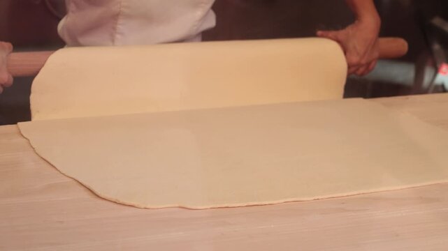 Pastry chef rolling out fresh dough with wooden pin