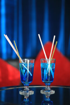 Two glasses of blue lagoon cocktail with plastic drinking straws on a mirror table in a nightclub or bar