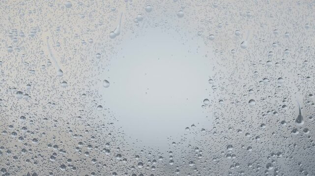 Forming water droplets on glass pane at window, rain intensifying and pulling streaks downward