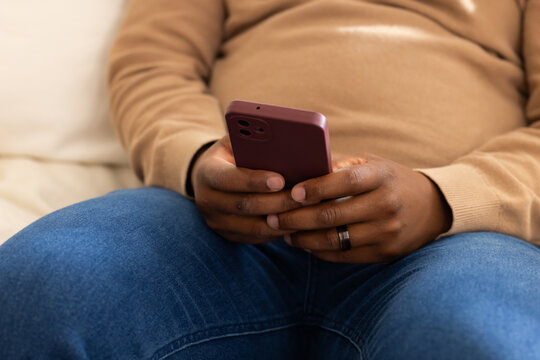 Man sitting on beige couch at home holding mauve dual-camera smartphone showing dark band ring