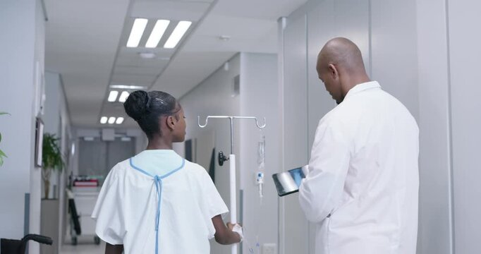 Doctor and youth patient walking hospital hall, tapping tablet reviewing xray, holding IV pole