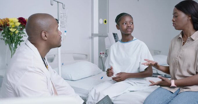 Teenage patient being prompted by mother talking while doctor listening with tablet in patient room