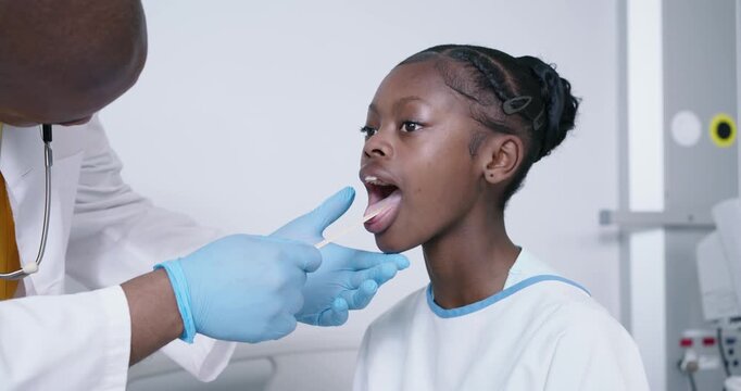 African American Dr instructing teen to open mouth for exam while examining throat with depressor