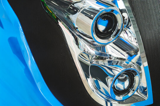 close-up of chrome car headlight. Two circular lenses dominate polished assembly. Shiny metal reflects light and surroundings clearly