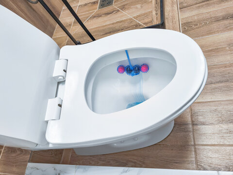 Open toilet bowl with blue cleaning block in tiled bathroom. Toilet cleaning and bathroom hygiene. Household sanitation and cleaning product use. Top view