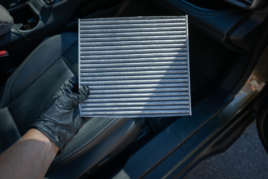 Gloved hand, holding a dirty cabin air filter in an automobile. Vehicle maintenance