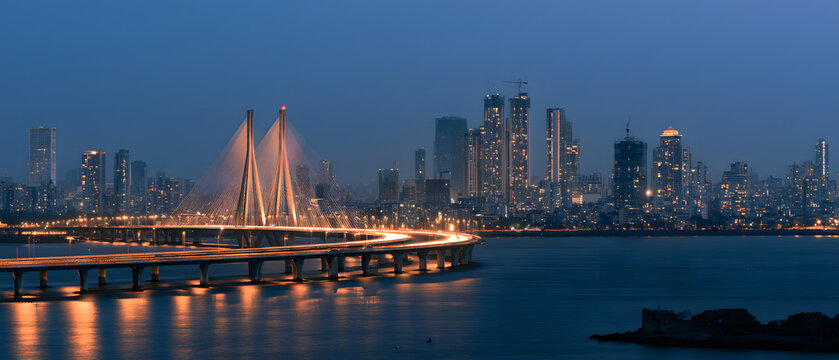 At evening, Mumbai's skyline gleams with the illuminated Bandra-Worli Sea Link bridge, while city lights reflect on the water, forming a modern cityscape of an Indian metropolis.