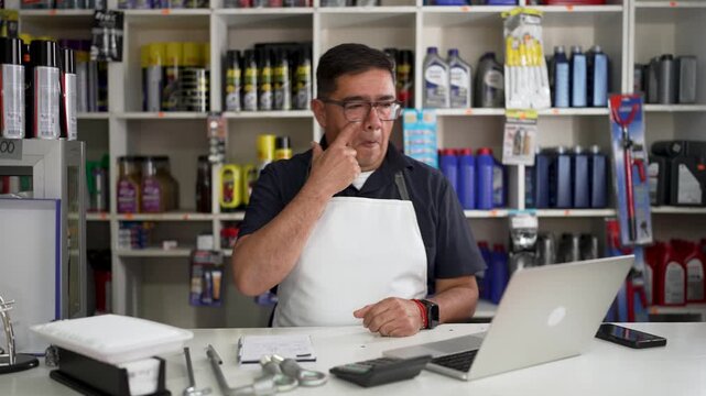 Mature latino mechanic wearing apron smiling and gesturing thumbs up behind workshop sales counter