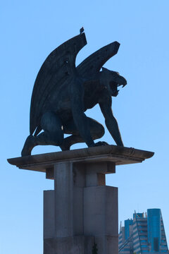 Bronze gargoyle sculpture perched on Pont del Regne bridge against blue sky in Valencia, Spain. Iconic urban guardian monument by Manolo Valdes