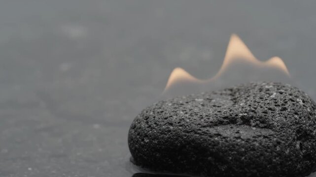 Macro close-up of dark textured volcanic basalt stone corner with subtle warm heat refraction shimmers against minimalist dark charcoal copy space for wellness spa