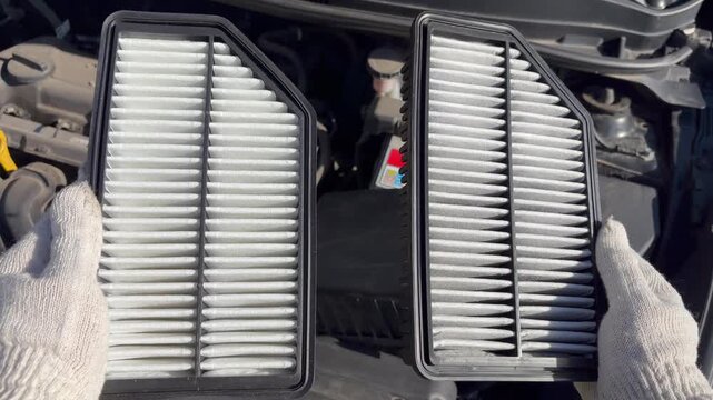 An auto mechanic is holding an old air filter and a new one. Automotive maintenance, DIY car repair, and routine vehicle servicing