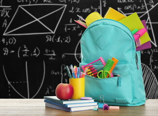 Backpack and school stationery on wooden table against chalkboard © New Africa