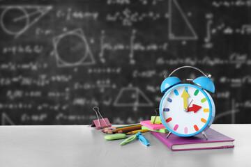 Alarm clock and school stationery on table against chalkboard © New Africa