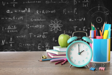 Alarm clock and school stationery on wooden table against chalkboard © New Africa