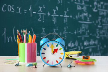 Alarm clock and school stationery on wooden table against chalkboard © New Africa