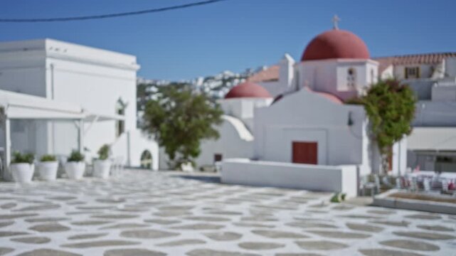 Mykonos church with red domes and whitewashed buildings, softly blurred plaza background; background backplate copyspace template.