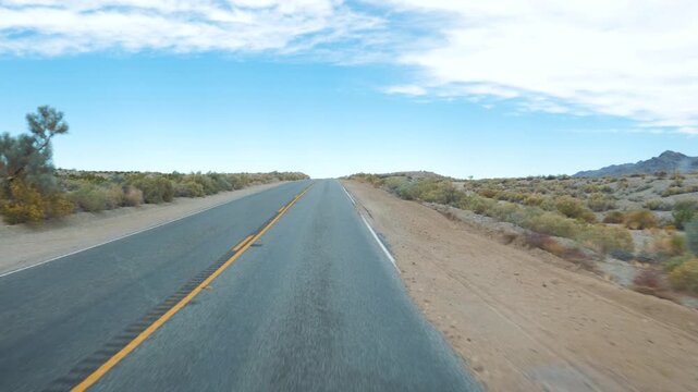 Vehicle driving along empty paved highway through arid desert landscape under bright sunny sky, offering front pov motion view of scenic route journey