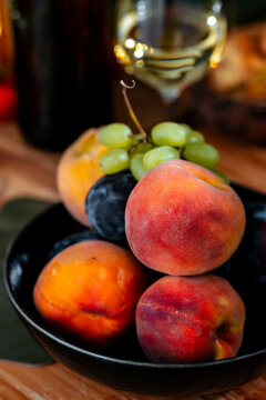 Fresh ripe peaches with green grapes in bowl and white wine glass - gourmet fruit appetizer pairing for friendly lunch. Mediterranean dinner table arrangement for catering event.